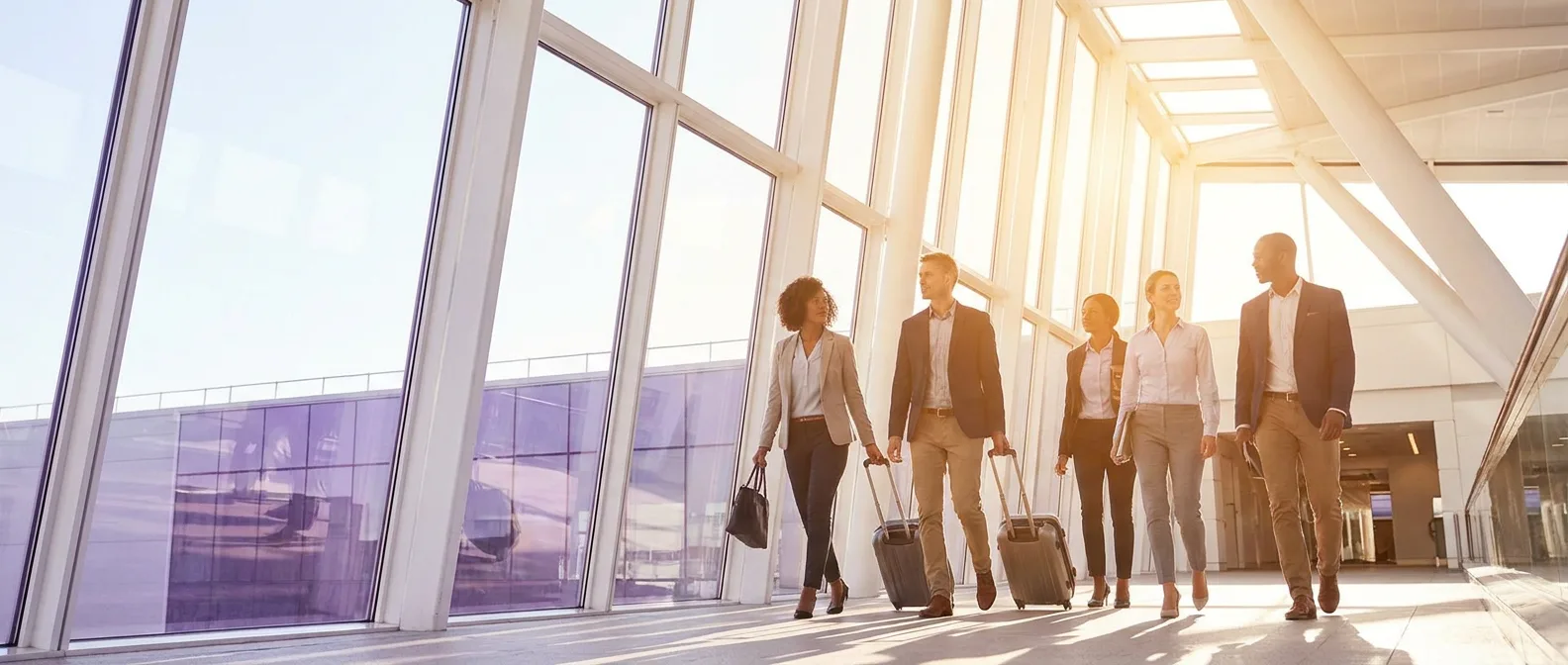 Business travellers with cabin bags walking through a sunlit, glass-walled airport concourse
